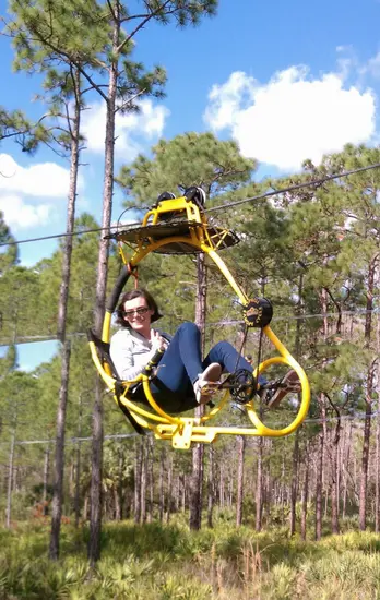 AirCruizer cable bicycle riders at treetop level in a forest setting